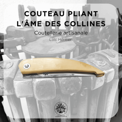 Couteau pliant artisanal intitulé "L'âme des collines" réalisé par Loïc Héritier, coutellerie artisanale. La lame en acier forgé brut de forge est finement polie, et le manche est en Buis du Luberon, offrant une prise en main ergonomique. Le couteau est posé sur un fond évoquant un atelier de forge artisanale, avec des outils en arrière-plan, mettant en valeur le savoir-faire de la coutellerie traditionnelle.