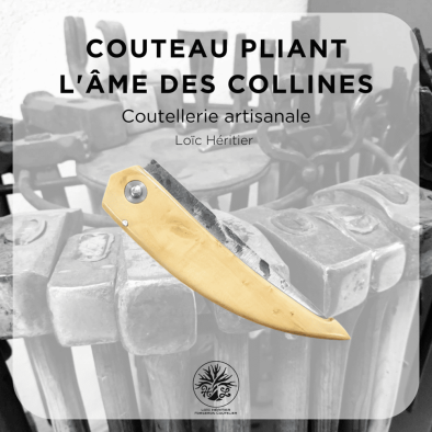 Couteau pliant artisanal intitulé "L'âme des collines" réalisé par Loïc Héritier, coutellerie artisanale. La lame en acier forgé brut de forge est finement polie, et le manche est en Buis du Luberon, offrant une prise en main ergonomique. Le couteau est posé sur un fond évoquant un atelier de forge artisanale, avec des outils en arrière-plan, mettant en valeur le savoir-faire de la coutellerie traditionnelle.
