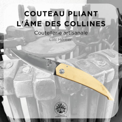 Couteau pliant artisanal intitulé "L'âme des collines" réalisé par Loïc Héritier, coutellerie artisanale. La lame en acier forgé brut de forge est finement polie, et le manche est en Buis du Luberon, offrant une prise en main ergonomique. Le couteau est posé sur un fond évoquant un atelier de forge artisanale, avec des outils en arrière-plan, mettant en valeur le savoir-faire de la coutellerie traditionnelle.