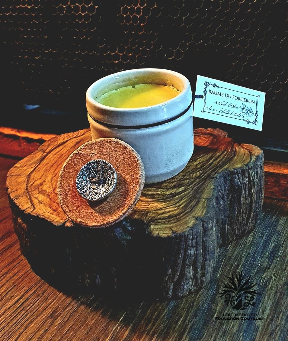 Image d'un pot de baume ouvert reposant sur une coupe transversale de tronc d'arbre, avec un couvercle en cuir embossé d'un symbole métallique, devant un fond de nid d'abeille.