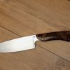 Élégance et précision définissent ce Couteau de Chef Artisanal, exposé sur un fond en bois clair qui met en valeur son esthétique raffinée. La lame, lisse et tranchante, est fabriquée en acier inoxydable X46Cr13, promettant une coupe impeccable et une résistance à la corrosion. Le manche en ronce de noyer de Provence, aux motifs tourbillonnants uniques, offre une prise en main confortable et une touche d'authenticité. La qualité de la fabrication artisanale française est mise en évidence par les rivets en acier qui accentuent l'aspect traditionnel et durable de ce couteau. Idéal pour les cuisiniers professionnels et les amateurs de gastronomie, ce couteau est un hommage à l'art culinaire.