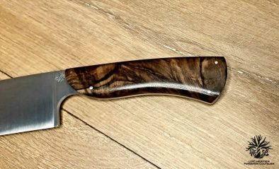 Élégance et précision définissent ce Couteau de Chef Artisanal, exposé sur un fond en bois clair qui met en valeur son esthétique raffinée. La lame, lisse et tranchante, est fabriquée en acier inoxydable X46Cr13, promettant une coupe impeccable et une résistance à la corrosion. Le manche en ronce de noyer de Provence, aux motifs tourbillonnants uniques, offre une prise en main confortable et une touche d'authenticité. La qualité de la fabrication artisanale française est mise en évidence par les rivets en acier qui accentuent l'aspect traditionnel et durable de ce couteau. Idéal pour les cuisiniers professionnels et les amateurs de gastronomie, ce couteau est un hommage à l'art culinaire.