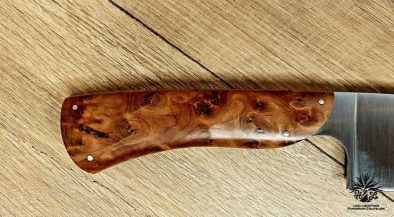 couteau de chef artisanal haut de gamme avec manche en bois du luberon . La lame est fabriquée en acier inoxydable robuste et finement affûtée, idéale pour une précision de coupe en cuisine. Le manche en bois de thuya présente des motifs de grain riches et une finition lisse avec des rivets en acier inoxydable, alliant esthétique traditionnelle et modernité. Cet outil de cuisine est à la fois fonctionnel et élégant, reflétant l'excellence de l'artisanat coutelier.